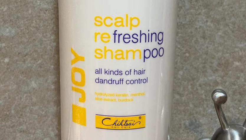 A white bottle reading "scalp refreshing shampoo". The letters of the words are in yellow and blue, such that the yellow blends in while the blue stands out. Due to how the color is split, the bottle appears to boldly declare "freshing poo".