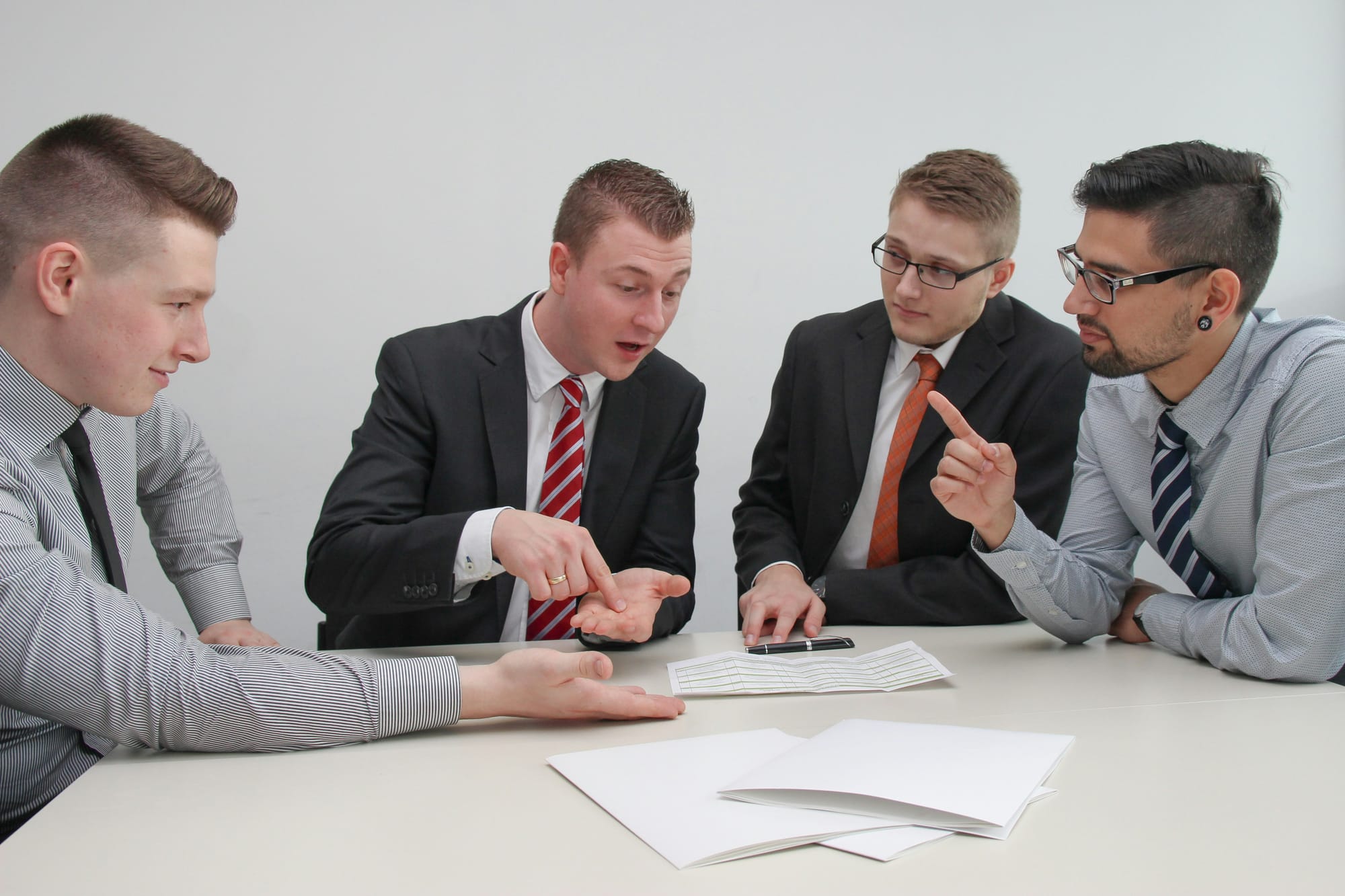 Four men in suits are having a stern, emphatic disagreement over some documents.